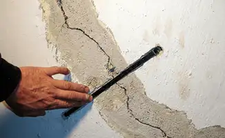 A wall with a large crack is being inspected by a professional in Des Moines, IA